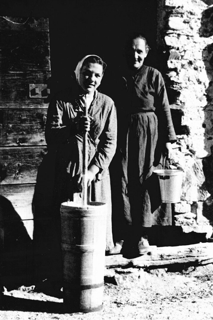 Madre e figlia in posa davanti alla porta della stalla, pronte per preparare il burro.